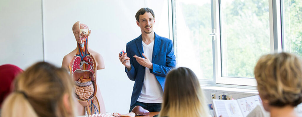 Dozent erklärt medizinische Zusammenhänge an einem Anatomie-Modell während des Pflegeunterrichts.