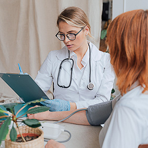 Pflegekraft misst den Blutdruck einer Patientin und notiert die Werte – Symbol für ambulante Pflegeassistenz.