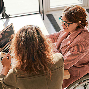 Zwei Frauen im Gespräch am Laptop – Symbol für Praxisberatung und individuelle Betreuung in der Pflege.